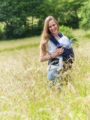 Porträt einer glücklichen Mutter, die ihre kleine Tochter im Tragetuch in der Natur trägt - LAF02040