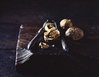 Close up of walnuts and nut cracker on wooden cutting board - CUF13898