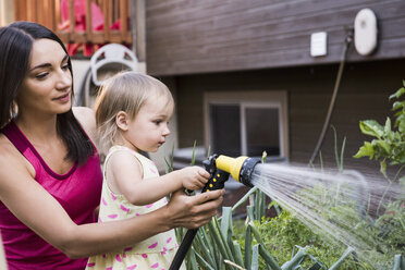 Mother and daughter in garden, watering plants together with hose - CUF13945