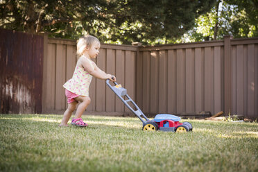 Junges Mädchen im Garten, das einen Spielzeugrasenmäher schiebt - CUF13977