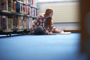 Junge Studentin schreibt Notizen auf dem Boden der Bibliothek - CUF13995