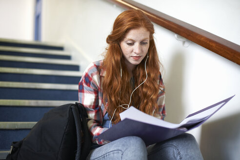 Junge Studentin sitzt auf einer Treppe und liest eine Akte - CUF14000