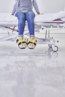 Low section of woman wearing bumblebee slippers sitting on hospital bed - CUF14013