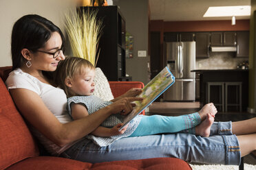 Mother teaching daughter to read book on sofa - CUF14017