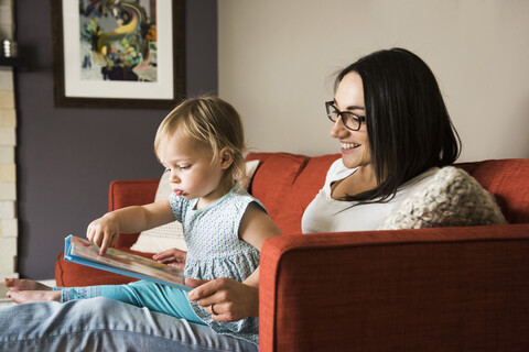 Mutter bringt ihrer Tochter auf dem Sofa das Lesen eines Buches bei, lizenzfreies Stockfoto