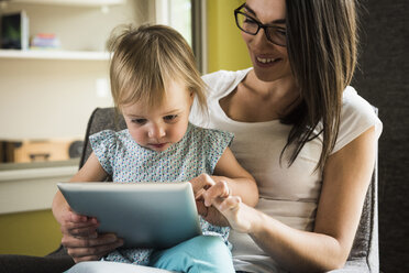 Mother teaching daughter to use digital tablet at home - CUF14020