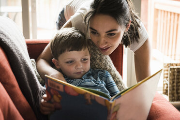 Mutter lehrt ihren Sohn auf dem Sofa ein Buch zu lesen - CUF14021