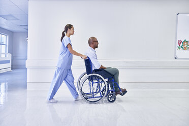 Arzt im Krankenhaus, der einen Patienten im Rollstuhl schiebt - CUF14046