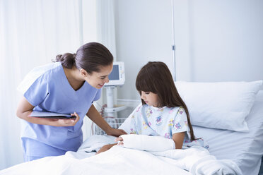 Eine Krankenschwester erklärt einem Mädchen mit Gipsarm auf der Kinderstation eines Krankenhauses etwas - CUF14064