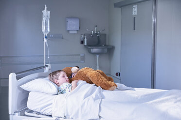 Boy patient in bed hugging teddy bear on hospital children's ward - CUF14081