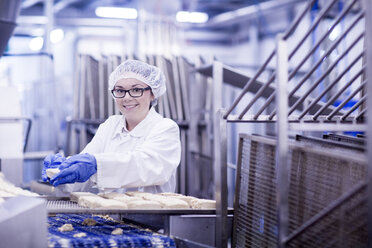 Frau arbeitet in einer Fabrik für Lebensmittelproduktion und schaut lächelnd in die Kamera - CUF14111