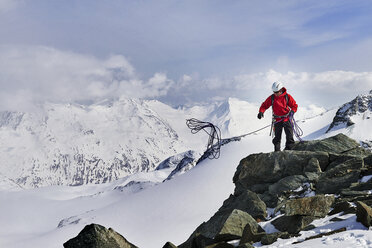 Mann auf dem Gipfel eines schneebedeckten Berges, der ein Kletterseil wirft, Saas Fee, Schweiz - CUF14194