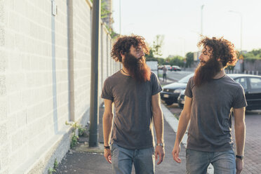 Eineiige männliche erwachsene Zwillinge schlendern und unterhalten sich auf dem Bürgersteig - CUF14209