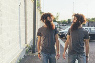 Identical male adult twins strolling and chatting on sidewalk - CUF14209