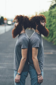 Porträt von eineiigen erwachsenen männlichen Zwillingen mit roten Haaren und Bärten Rücken an Rücken auf dem Bürgersteig - CUF14215