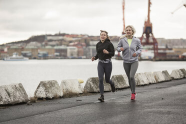 Two female runner friends running along dockside - CUF14270