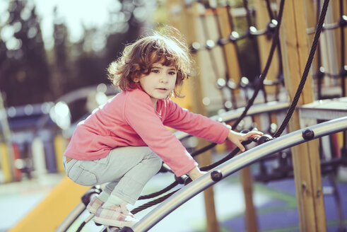 Porträt eines kleinen Mädchens, das auf einem Klettergerüst auf einem Spielplatz kauert - JSMF00207