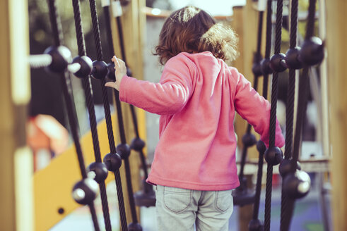 Rückansicht eines kleinen Mädchens auf einem Klettergerüst auf einem Spielplatz - JSMF00209