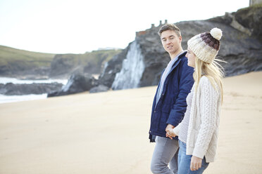 Young couple strolling hand in hand on beach, Constantine Bay, Cornwall, UK - CUF14341