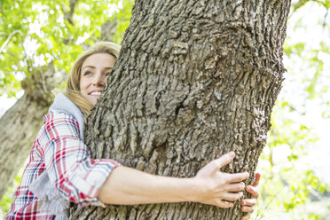 Frau umarmt lächelnd einen Baum - CUF14422