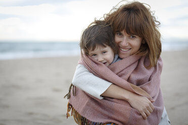 Mother and daughter wrapped in blanket hugging on beach - CUF14445