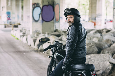 Portrait of mature male motorcyclist looking over his shoulder from motorcycle under flyover - CUF14461