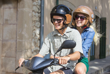 Young couple riding moped together through village, Majorca, Spain - CUF14482