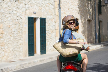 Young woman riding pillion through village looking back, Majorca, Spain - CUF14483