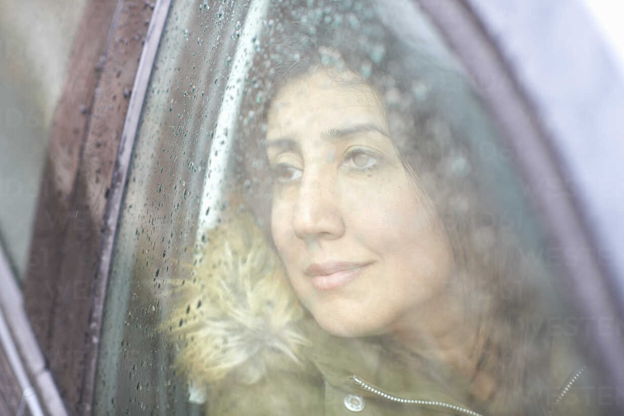 Reife Frau blickt durch Autofenster im Regen, lizenzfreies Stockfoto