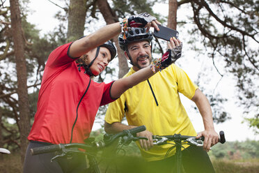 Glückliches Mountainbike-Paar nimmt Smartphone-Selfie im Wald - CUF14493