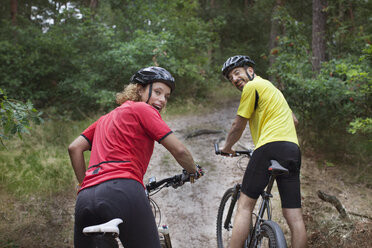 Porträt eines Mountainbike-Paares, das sich im Wald über die Schultern schaut - CUF14496