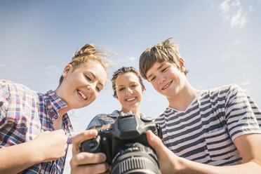 Niedriger Blickwinkel auf einen jungen Mann und seine Freundinnen, die Fotos vor der Kamera prüfen - CUF14540