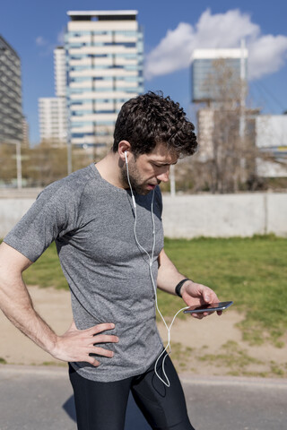 Sportlicher Mann mit Handy und Kopfhörern in städtischem Gebiet, lizenzfreies Stockfoto