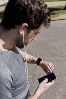 Sportlicher Mann mit Handy, Kopfhörer und Smartwatch im Freien - MAUF01396
