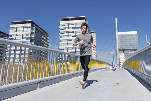 Sportlicher Mann beim Laufen auf einer Brücke in der Stadt - MAUF01403