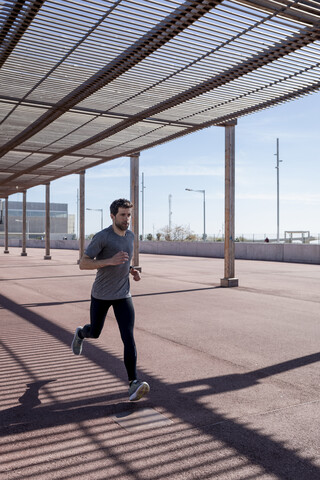 Sportlicher Mann beim Laufen unter einer Überdachung in der Stadt, lizenzfreies Stockfoto