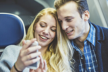 Young couple reading smartphone texts in train carriage - CUF14610