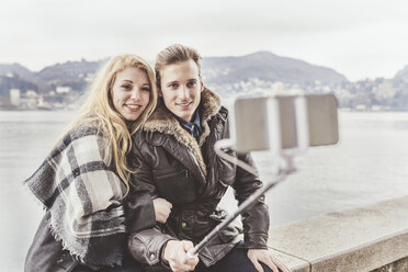 Young couple taking smartphone selfie on harbour wall, Lake Como, Italy - CUF14621