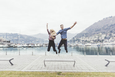 Young couple on waterfront jumping mid air, Lake Como, Italy - CUF14623