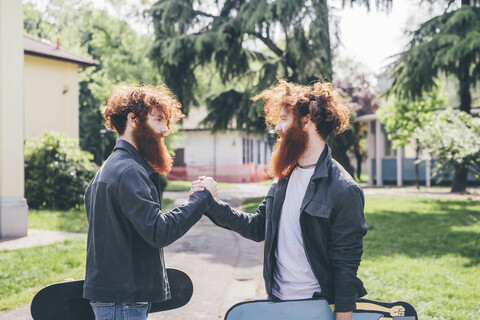 Junge männliche Hipster-Zwillinge mit roten Bärten schütteln Hände im Park, lizenzfreies Stockfoto