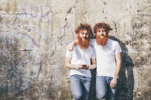 Portrait of young male hipster twins with red beards standing in front of wall - CUF14650