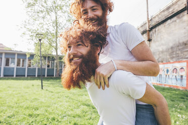 Young male hipster twins with red beards piggy backing in park - CUF14652