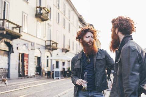 Junge männliche Hipster-Zwillinge mit roten Haaren und Bärten unterhalten sich auf einer Straße in der Stadt, lizenzfreies Stockfoto