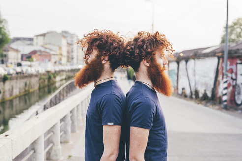 Portrait of young male hipster twins with red hair and beards back to back on bridge - CUF14666