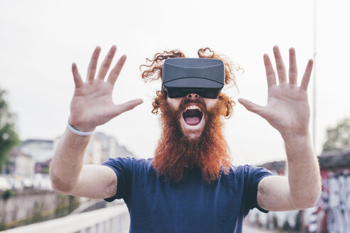 Portrait of young male hipster with red hair and beard screaming whilst wearing virtual reality headset - CUF14667