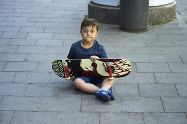 Porträt eines staunenden kleinen Jungen, der mit einem Skateboard auf dem Bürgersteig sitzt - BEF00105