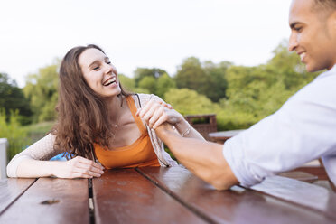 Young couple arm wrestling on picnic bench laughing - CUF14805