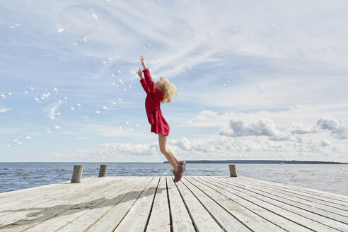 Junges Mädchen auf Holzsteg, das springt, um Luftblasen zu erreichen - CUF14829
