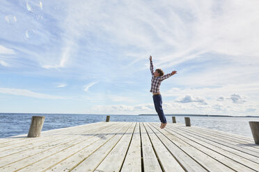 Young boy on wooden pier, jumping to reach bubbles - CUF14830