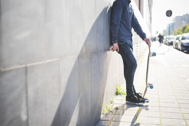 Junger männlicher Skateboarder lehnt an einer Mauer auf dem Bürgersteig - CUF14849